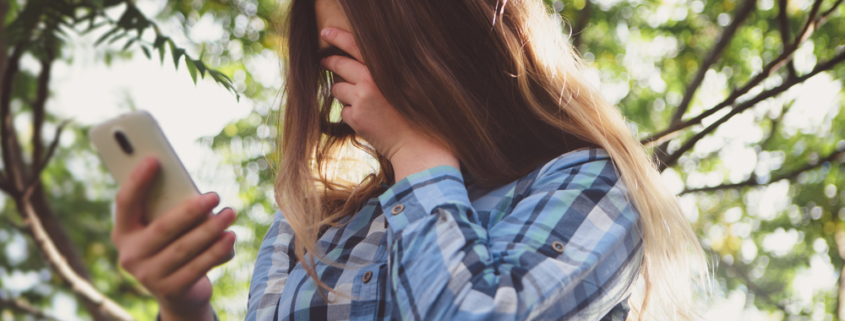 Image of a girl looking at her smartphone while covering her face with her other hand