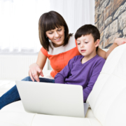 Image of a young boy sitting on the sofa with his mother in front of a laptop