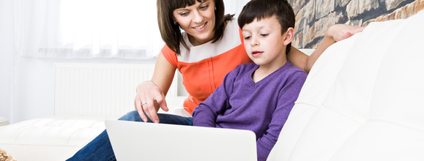 Image of a young boy sitting on the sofa with his mother in front of a laptop