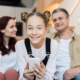 Image of a smiling girl with a smartphone in her hands and her parents in the background blurry and smiling