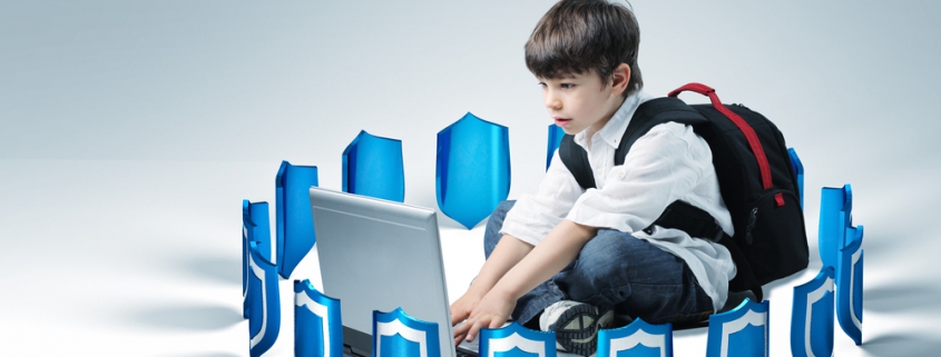 Image of a young boy sitting on the floor with his backpack on and typing on a laptop while being surrounded with small blue / silver shields.