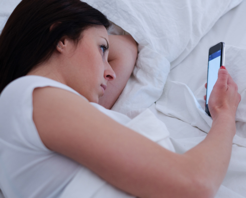 Image of a serious young woman lying in bed and looking at her smartphone