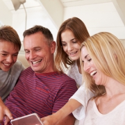 Image of a family (son, father, daughter and mother) all smiling and pointing at a smartphone