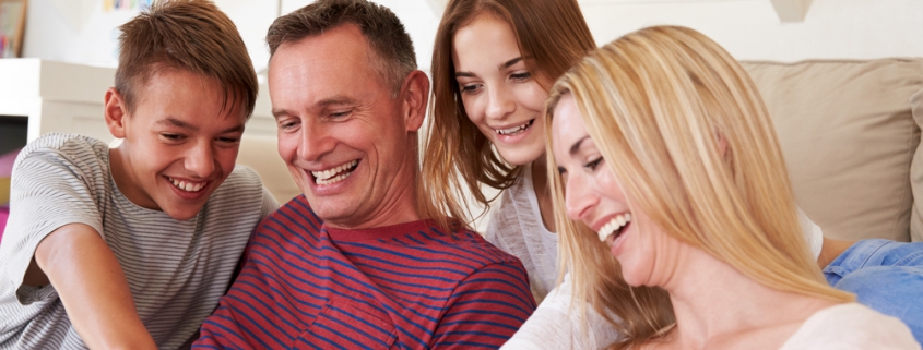 Image of a family (son, father, daughter and mother) all smiling and pointing at a smartphone