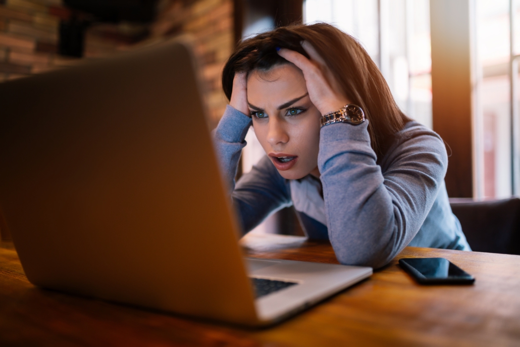 Image of teen girl sitting in front of the laptop and holding her head in her hands looking worried