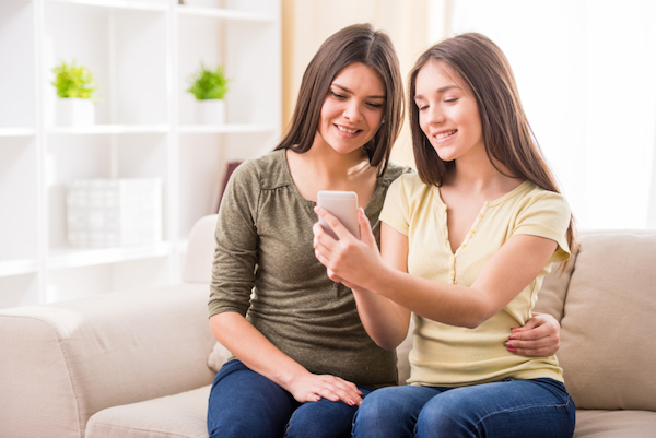 Image of mother and daughter looking at the smartphone the daughter is holding in her right hand and smiling