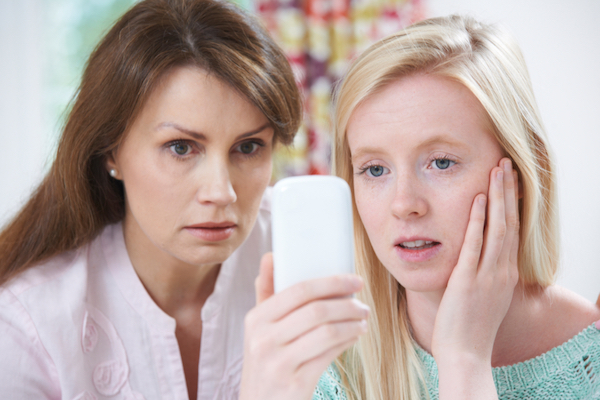 Image of mother and daughter looking worrying at the smartphone the daughter is holding in her right hand